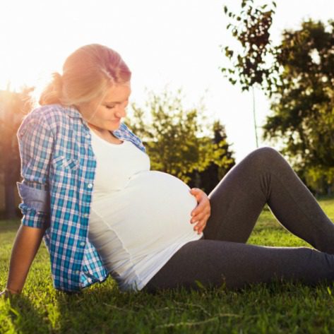 A blonde pregnant woman sitting and wondering about adoption for her baby