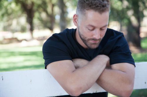 Young birthfather leans on a fence